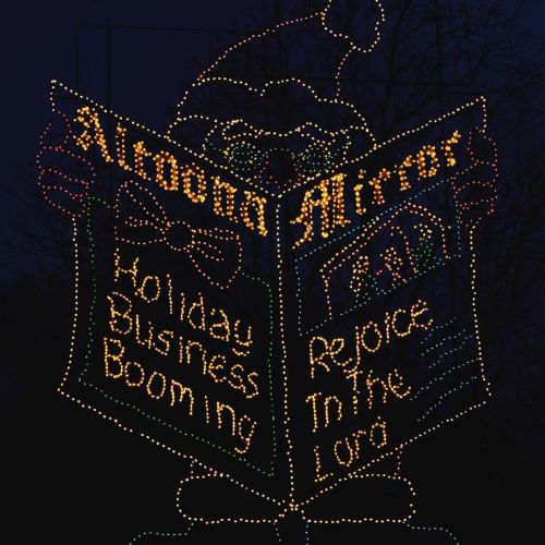 A festive display featuring a large book with lights, reading "Holiday Business Booming" and "Rejoice in the Lord."
