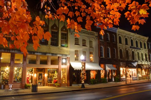 Charming street lined with shops, illuminated at night, framed by vibrant autumn leaves.
