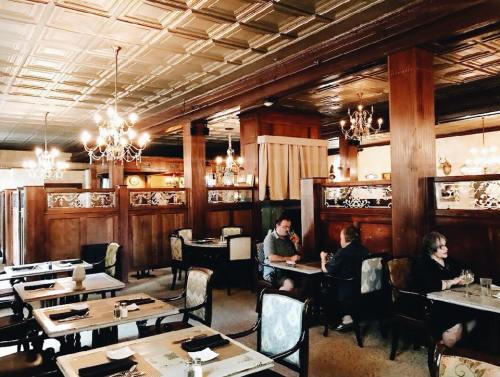 Elegant restaurant interior with wooden decor, chandeliers, and patrons dining at tables.