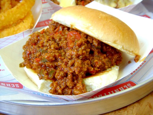 A close-up of a sloppy joe sandwich filled with seasoned ground meat and served on a soft bun.
