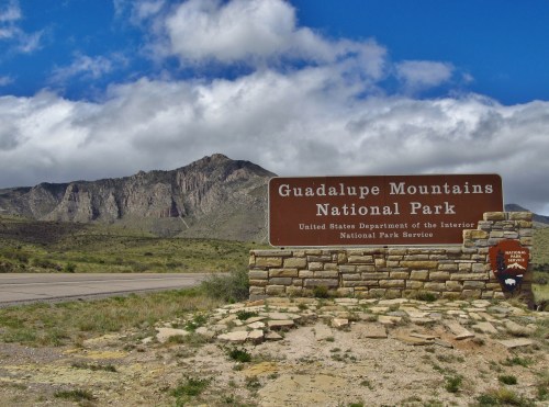 Sign for Guadalupe Mountains National Park with mountains and cloudy sky in the background.