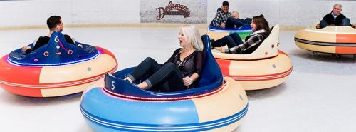 People enjoying bumper cars on ice, smiling and having fun in colorful, circular vehicles.