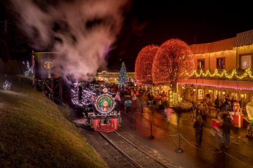 A festive train station at night, adorned with holiday lights and a Christmas tree, bustling with cheerful visitors.