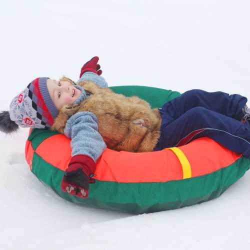 A child in winter clothing sits in a colorful snow tube, smiling and enjoying a snowy landscape.