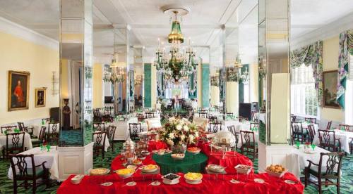 Elegant dining room with chandeliers, mirrors, and a buffet table adorned with flowers and various dishes.