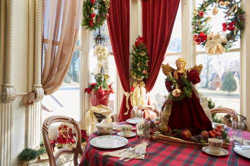 A festive dining table decorated with holiday ornaments, an angel figurine, and seasonal greenery by a sunny window.