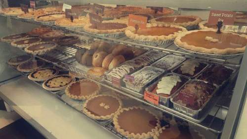 A display case filled with various pies, including pumpkin and sweet potato, alongside donuts and dessert cups.