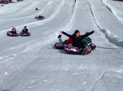 A group of people enjoying snow tubing on a snowy slope, with one person joyfully raising their arms.