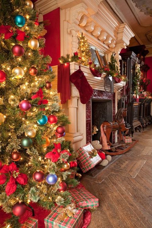 A beautifully decorated Christmas tree with ornaments, gifts, and a festive fireplace adorned with stockings and greenery.