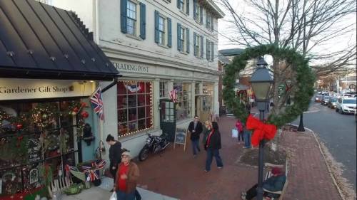 A festive street scene with holiday decorations, shoppers, and a wreath hanging on a lamp post.
