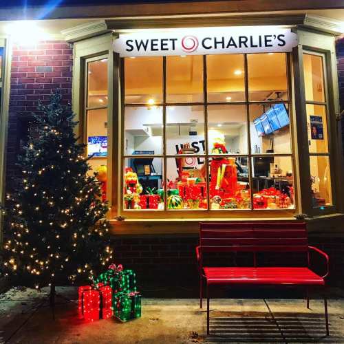 A festive storefront of Sweet Charlie's with a decorated tree, gifts, and a red bench outside.