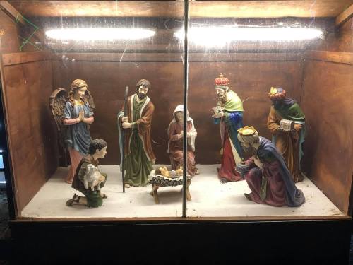 A nativity scene displayed in a glass case, featuring figures of Mary, Joseph, baby Jesus, and the Three Wise Men.