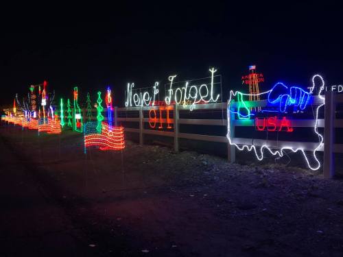 Colorful holiday lights display featuring trees and the text "Never Forget" and "USA" against a dark night sky.