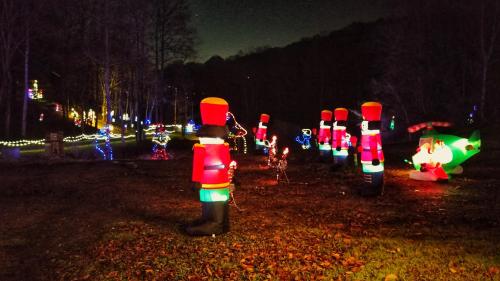 Colorful holiday decorations featuring toy soldiers and festive lights in a dark, wooded area.