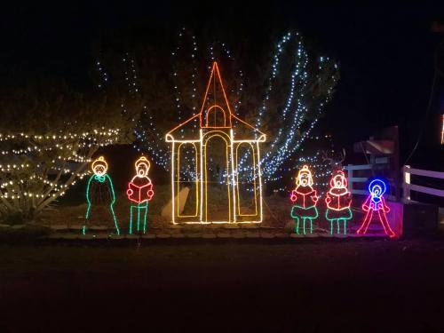 Colorful holiday lights depicting a church and carolers in a festive nighttime setting.
