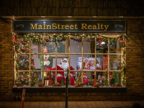 A festive realty office window decorated for Christmas, featuring Santa, a mannequin, and holiday lights.