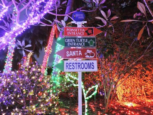 A colorful signpost with arrows pointing to various attractions, surrounded by festive holiday lights.