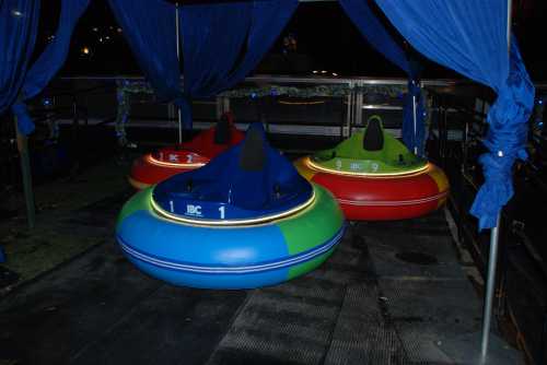 Three colorful bumper boats are lined up under a blue canopy, with lights glowing around their bases.