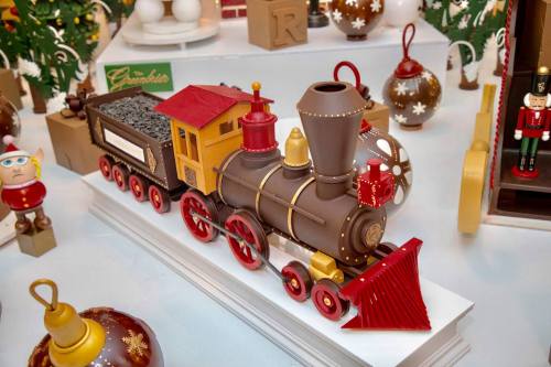 A decorative toy train with a red and yellow engine, surrounded by festive ornaments and holiday decorations.