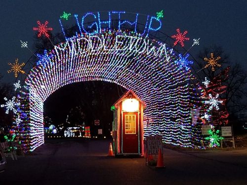 Colorful holiday lights form an archway with "Light Up" above and a small booth at the entrance, set against a twilight sky.