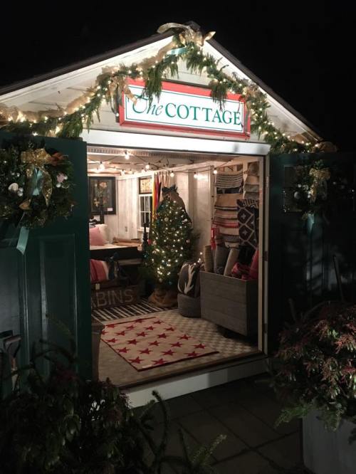 A cozy cottage decorated for the holidays, featuring a Christmas tree and festive garlands, illuminated at night.