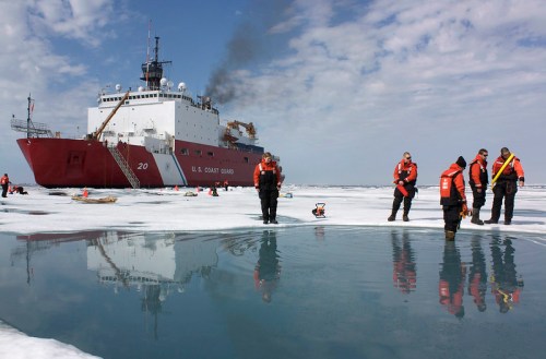 U.S. Coast Guard ship in icy waters with crew members in orange jackets examining the ice.