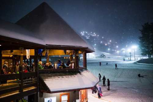 A snowy night scene at a ski resort, with a bustling lodge and illuminated slopes in the background.