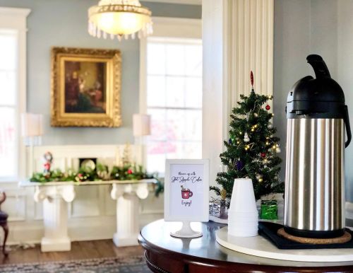 A cozy room decorated for the holidays, featuring a coffee dispenser, a sign, and a small Christmas tree.