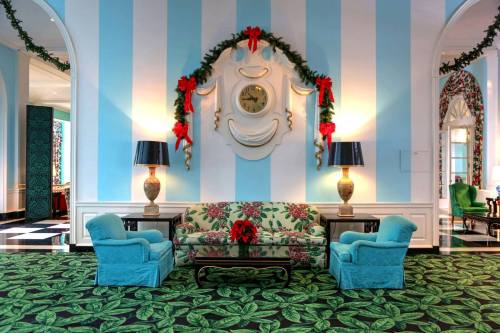 A festive lobby with blue striped walls, floral furniture, and holiday decorations, including garlands and bows.