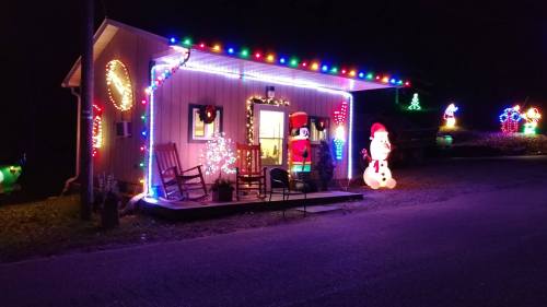 A cozy cabin decorated with colorful Christmas lights, featuring a snowman and Santa outside.