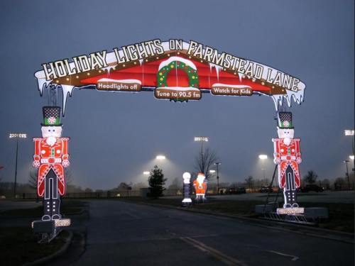 A festive archway with nutcracker figures, announcing "Holiday Lights on Farmstead Lane" and radio tune-in details.
