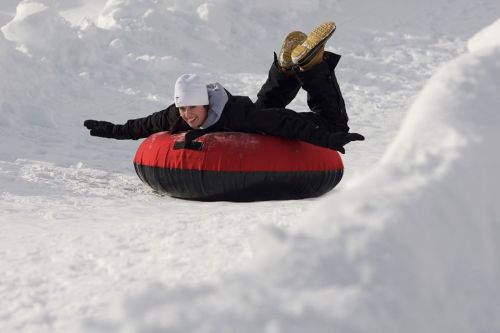 A person in winter gear joyfully sleds down a snowy hill on a red and black inflatable tube.