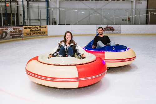 Two people sit in colorful bumper cars on an ice rink, smiling and enjoying their time.