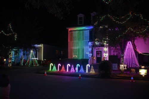 A brightly lit house decorated with colorful Christmas lights, featuring trees and festive designs in a nighttime setting.