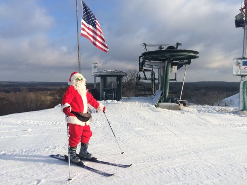 Santa Claus skiing on a snowy slope with an American flag and ski lift in the background.