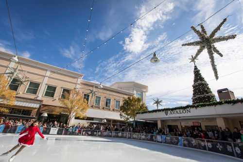 A figure skater in a red dress glides on an ice rink, with holiday decorations and a crowd in the background.