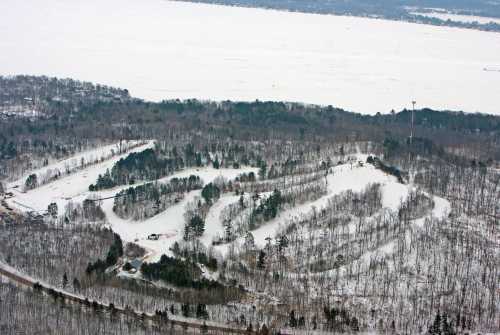 Aerial view of snow-covered hills and trees, with a frozen lake in the background.