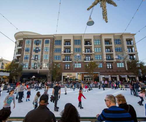 A bustling outdoor ice skating rink with families and children skating, surrounded by shops and festive decorations.