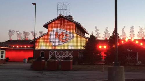 A brightly lit building featuring the Kansas City Chiefs logo, with festive decorations on the roof at dusk.