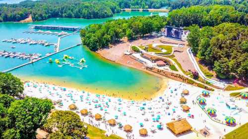 Aerial view of a vibrant beach with people, boats, and green trees surrounding a calm lake and recreational area.