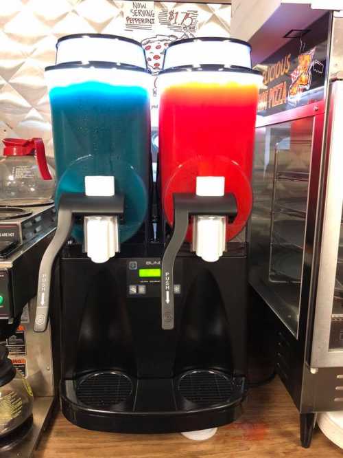 Two slushie machines with blue and red slushies, positioned side by side, in a food service area.