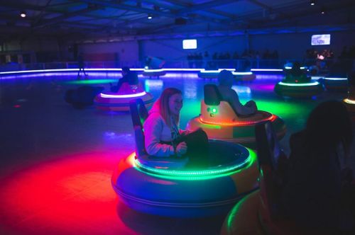 A dimly lit indoor space with colorful bumper cars and people enjoying a fun ride under vibrant lights.