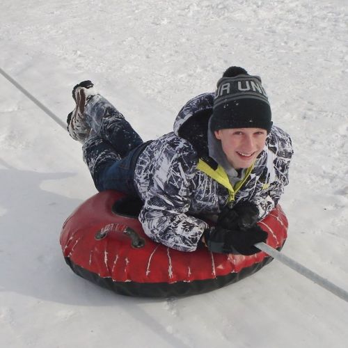 A young person in a winter jacket and hat is tubing down a snowy slope, smiling as they hold onto the tube.