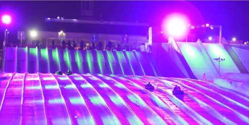 Colorful lights illuminate a snowy slope where people are sledding down on tubes.