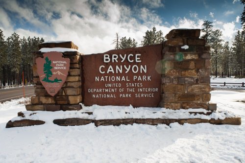 Sign for Bryce Canyon National Park, featuring stone structure and snowy landscape, with trees in the background.