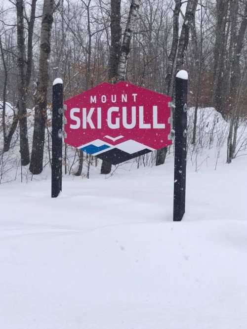 Sign for Mount Ski Gull surrounded by snow-covered trees in a winter landscape. Snow is falling gently.