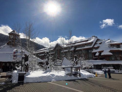 A snowy landscape with a large building, trees, and a bright sun in a clear blue sky.