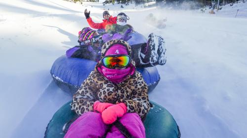 A group of children in colorful winter gear tubing down a snowy hill, smiling and enjoying the fun.