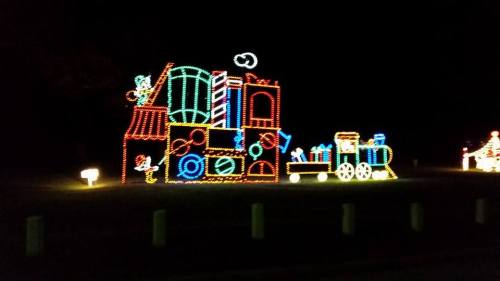 Colorful holiday lights display featuring a train and various toy-themed decorations against a dark night sky.
