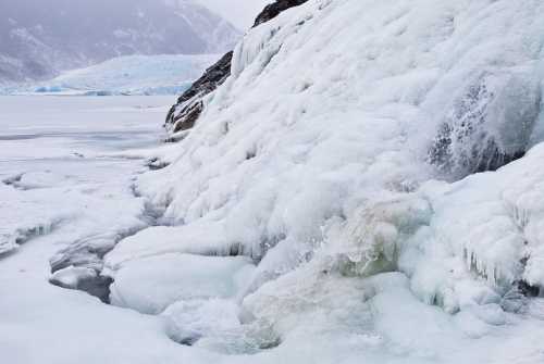 A frozen landscape featuring icy cliffs and a partially frozen waterfall, with a snowy backdrop.